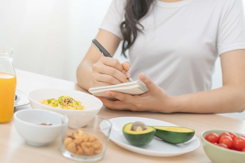 Woman taking notes while eating a healthy meal